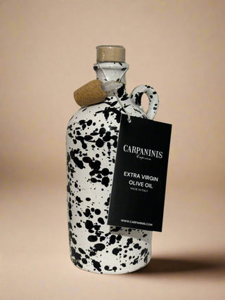 A Carpaninis bottle of olive oil from Italy. Painted white with a black splatter on a sandstone background.