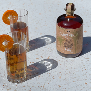 carpaninis organic rum bottle with two high ball rum glasses in the sun