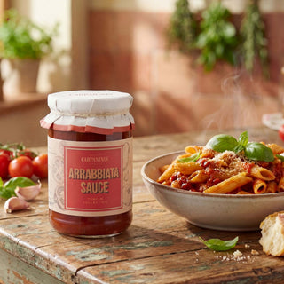 A jar of arrabbiata pasta sauce next to a bowl of penne pasta