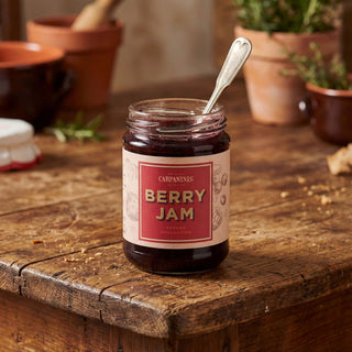 A jar. ofberry jam on a wooden table with a spoon inside