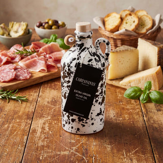 A Carpaninis handmade olive oi on a wooden table surrounded by a cheeseboard