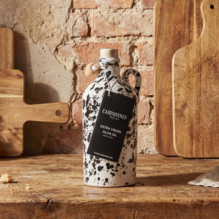 Decorative olive oil bottle with speckled design and 'Carpaninis' label on a rustic wooden surface.
