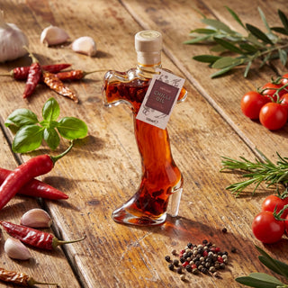 An Italy shaped bottle of chilli oil on a wooden table surrounded by chillies