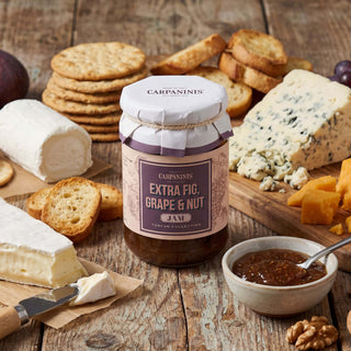 A jar of Carpaninis fig jam on a wooden table surrounded by a cheesboard