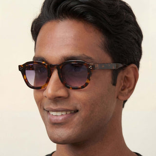 Man wearing tortoiseshell sunglasses with a neutral background