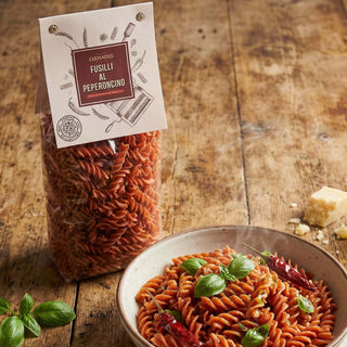 Packaged fusilli pasta with a bowl of fusilli al peperoncino on a wooden surface.