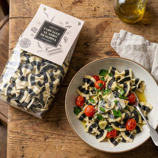 Packaged pasta next to a bowl of pasta salad on a wooden table
