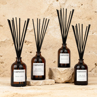 Four Carpanini diffusers with black reeds against a stone wall background