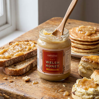 A jar of Carpaninis Welsh set honey on a wooden table spread on toast and pancakes