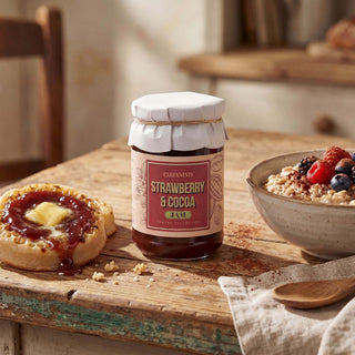 A jar of Carpaninis strawberry jam on a wooden table with a crumpet and porridge