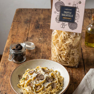 Truffle tagliatelle pasta with a jar of truffles and a package of pasta on a wooden table.