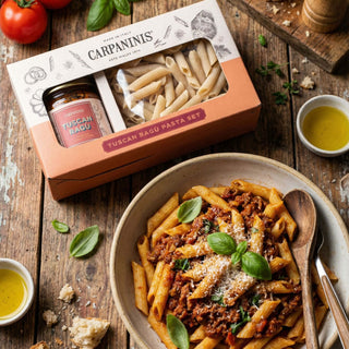 A gift pack of penne and Tuscan ragu sauce on a table nxt to a prepared bowl