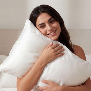 Woman holding a white pillow with 'Carpaninis' branding, smiling in a bedroom setting.