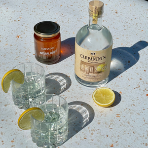 a bottle of carpaninis gin alongside carpaninis honey and two glasses in the sunshine