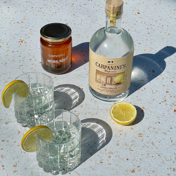 carpaninis lemon and honey gin in the sun with two glasses and a jar of carpaninis honey